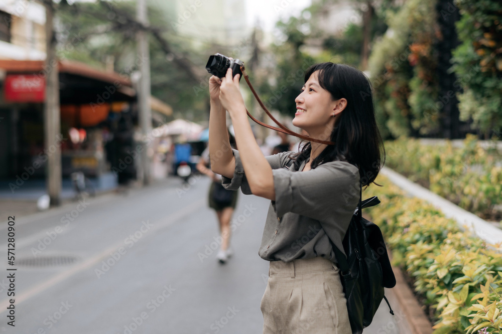 Young Asian woman backpack traveler using digital compact camera, enjoying street cultural local place and smile. Traveler checking out side streets. Journey trip lifestyle, world travel explorer
