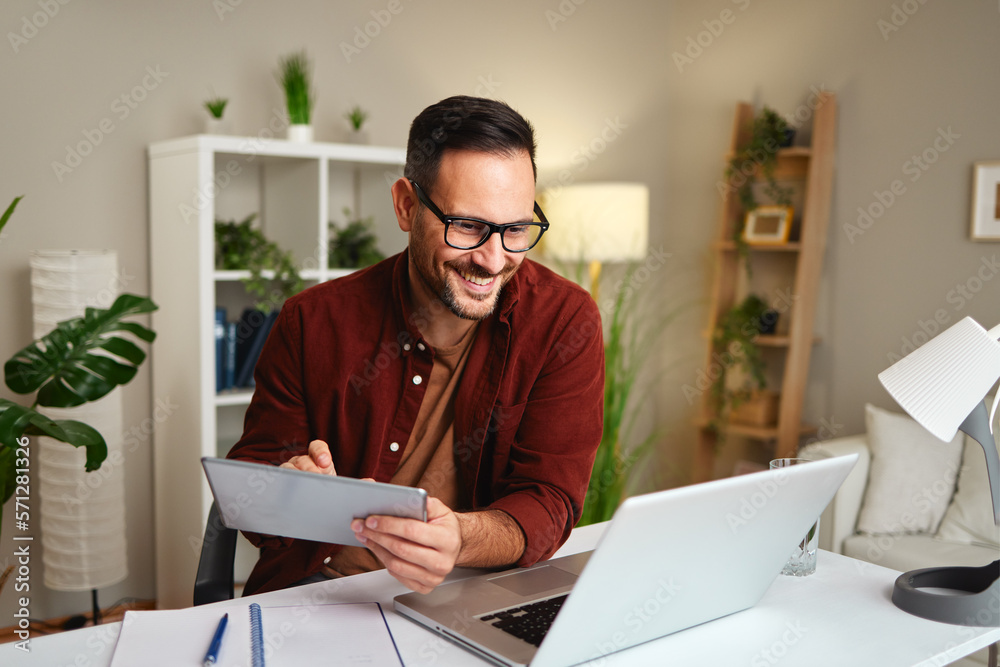 Young man works from home at a desk with a tablet and a laptop Young man works from home at a desk with a tablet and a laptop