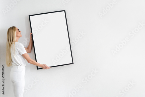 happy woman hanging picture on wall in room photo