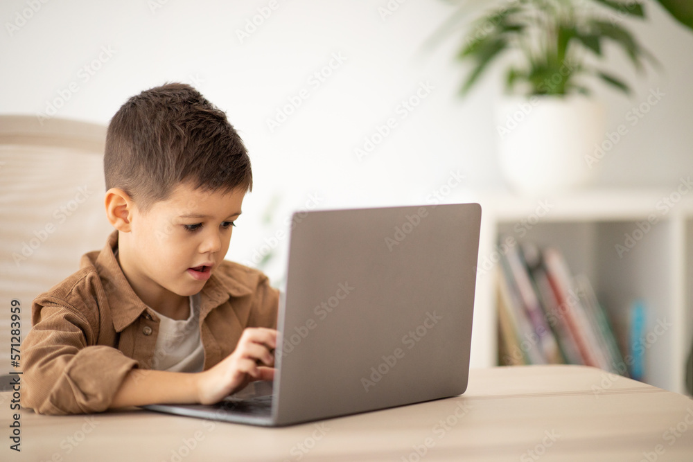 Busy cute european small kid typing on laptop at table, watch video lesson, play game, has meeting Busy cute european small kid typing on laptop at table, watch video lesson, play game, has meeting