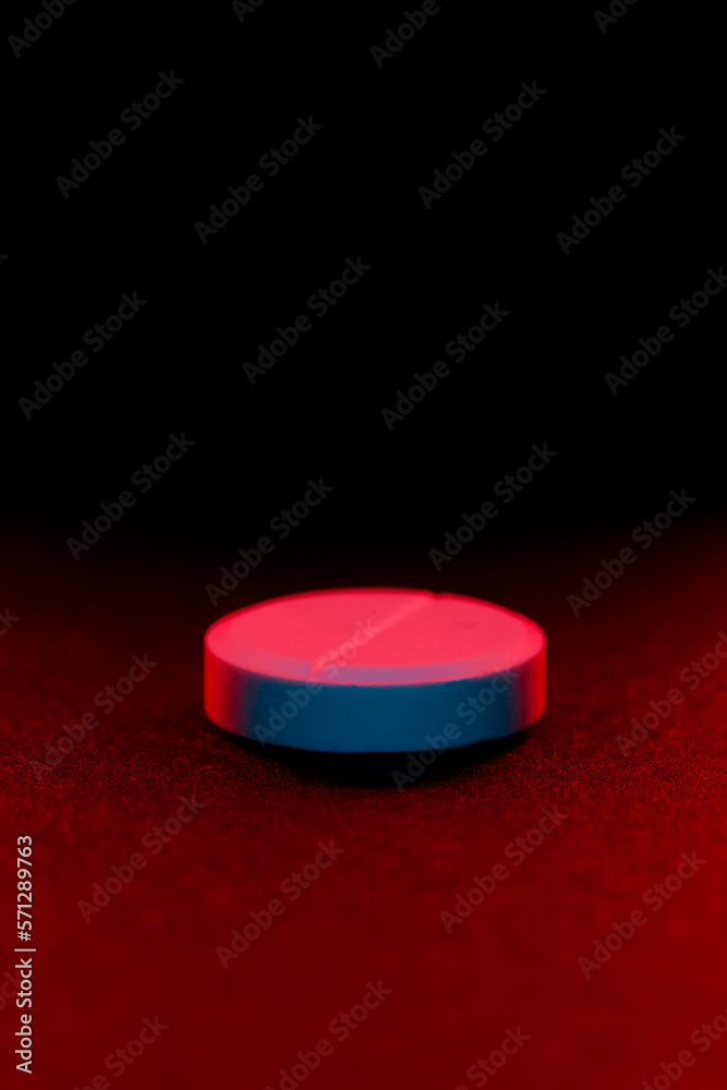 Toxic and poison pharmacy concept. Close up of white pill on black background lit with red. Toxic and poison pharmacy concept. Close up of white pill on black background lit with red.