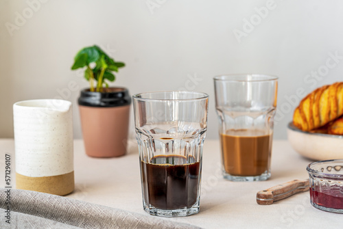 Spring cozy breakfast concept. Two glasses with coffee and milk, croissants, spring plant, jam, linen napkin. Kinfolk style