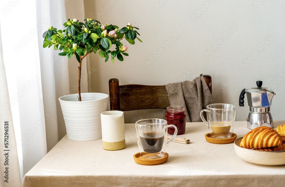 Spring cozy breakfast concept. Two mugs with coffee and milk, croissants, plant with flowers, creamer, coffee pot, jam Spring cozy breakfast concept. Two mugs with coffee and milk, croissants, plant with flowers, creamer, coffee pot, jam
