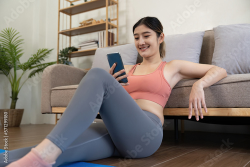 young woman exercising at home happily sitting and resting playing on the phone