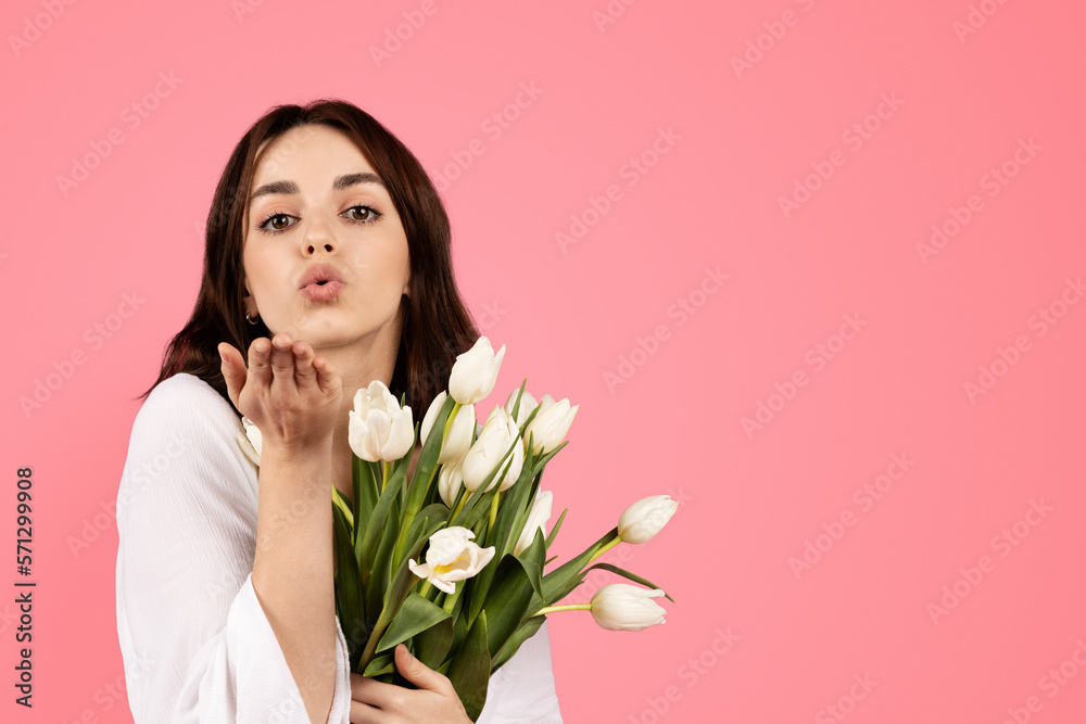 Smiling young european woman with bouquet of white tulips making blowing kiss, enjoy lifestyle, spring holiday Smiling young european woman with bouquet of white tulips making blowing kiss, enjoy lifestyle, spring holiday