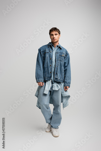 full length of young man in denim outfit posing and looking at camera on grey.