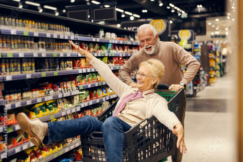 Fotografia A funny old couple is driving in shopping cart at the supermarket