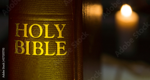 Holy Bible in close-up and a lit candle at the background disfocused photo