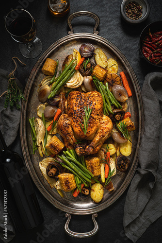 Appetizing roasted chicken with vegetables on a platter.  Dark background. Top view.