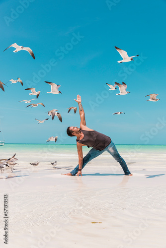 Man practicing yoga on the beach surrounded by seagulls