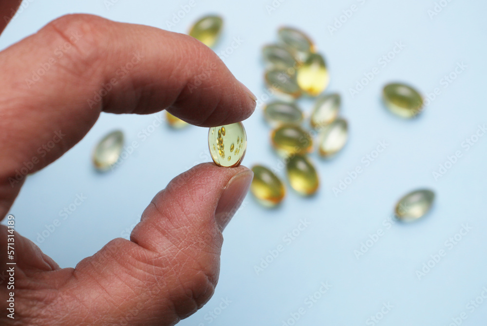 A man's hand holds a yellow capsule with fish oil close-up.
A man's hand holds a yellow capsule with fish oil close-up.