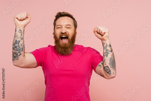 joyful bearded man with closed eyes showing triumph gesture and screaming isolated on pink.