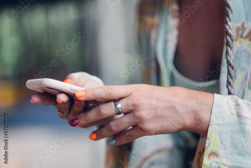 Fashionable woman with colorful nail polish checks social networks on phone.
