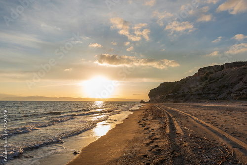 Beach with sand and rocks on sunset with sun light and clouds on sky