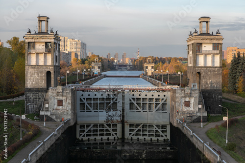 City water sluice gate on the Moscow canal with technical concrete dam buildings. Closed metal gates hold millions of tons of water from Moskva River. Urban landscape of the metropolis is around.