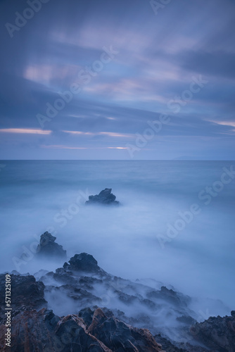 Long exposure shot of rocks on seaside, blurred and foggy sea water and clouds on sky © Aytug Bayer