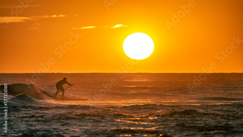 Silhouette of a man practicing paddle surfing on a wave in the sea with the sunset and the sun sphere in the background. Castelldefels, Barcelona. photo