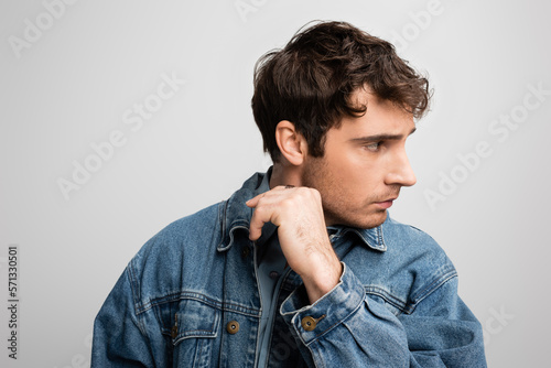 young model in denim jacket posing and looking away isolated on grey. © LIGHTFIELD STUDIOS