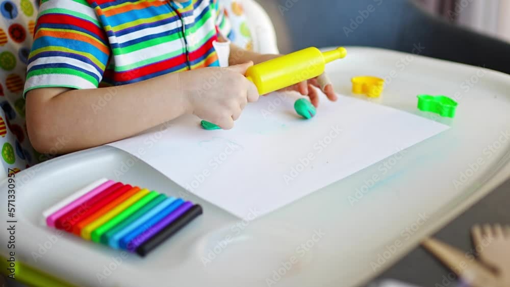 Little girl plays with multi-colored plasticine, creates different shapes with toy rolling pin Little girl plays with multi-colored plasticine, creates different shapes with toy rolling pin