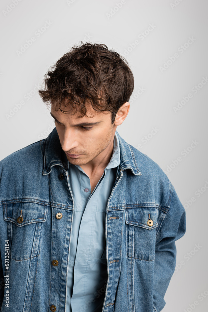 young man in denim jacket looking away while posing isolated on grey.