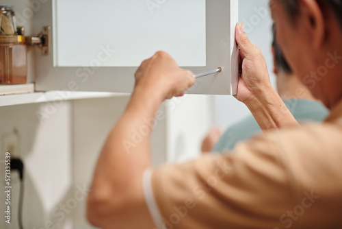 Senior woman fixing door of kitchen cabinet