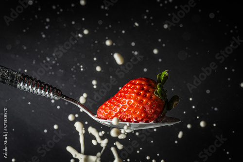 Makrofoto einer Erdbeere, die in einen Löffel voller Milch fällt