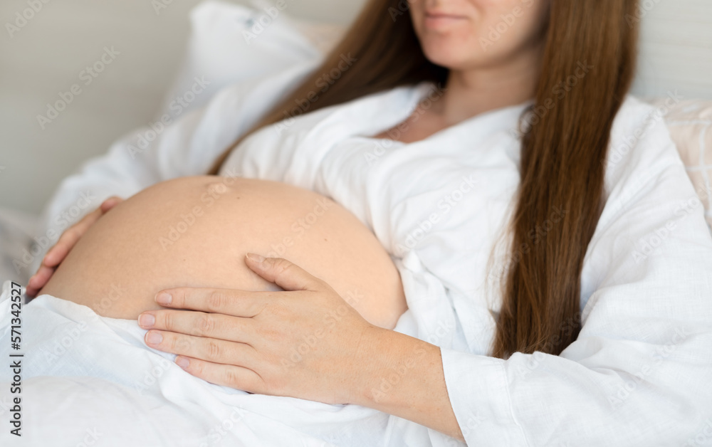 Unrecognizable pregnant woman lying on bed at home caressing,stroking belly, baby bump.Cropped, close-up shot.Happy beautiful pregnancy.Love to future child concept. Unrecognizable pregnant woman lying on bed at home caressing,stroking belly, baby bump.Cropped, close-up shot.Happy beautiful pregnancy.Love to future child concept.