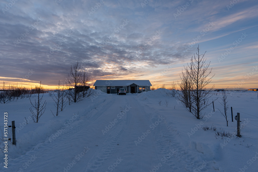 Secluded house in the snow with the ground and the road completely snow covered in residential area of Selfoss in Iceland with the cloudy sky illuminated by the first rays of the sun Secluded house in the snow with the ground and the road completely snow covered in residential area of Selfoss in Iceland with the cloudy sky illuminated by the first rays of the sun