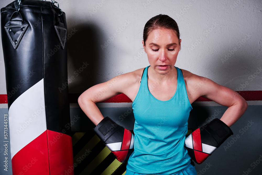 Sporty woman with boxing gloves standing next to the punching bag at the gym.