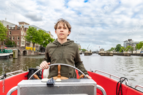 A boy at the wheel of a boat on a canal in Amsterdam