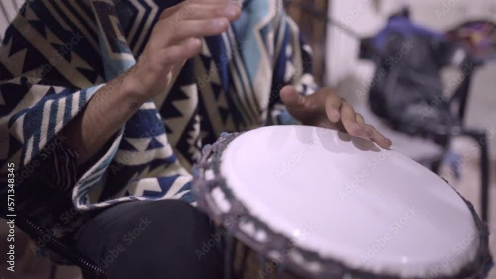 A young male playing djembe drums in a mexican jam session wearing a poncho