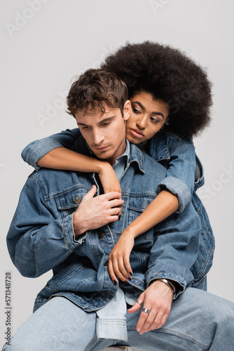brunette african american woman leaning on young man in denim outfit isolated on grey.