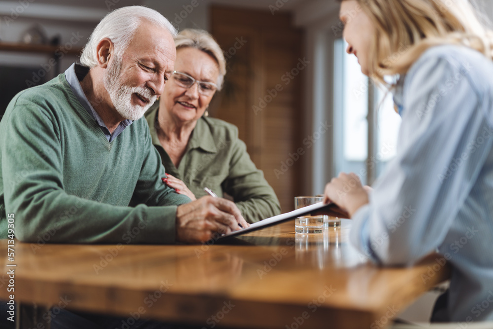 Happy senior couple signing a document with their financial advisor at home - obrazy, fototapety, plakaty 