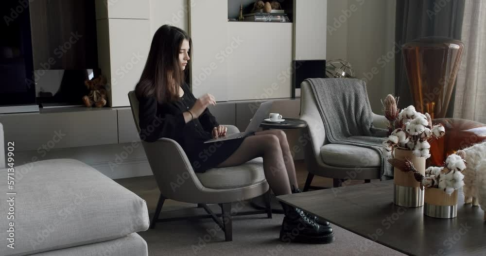 Pretty young Caucasian woman texting on the keyboard of the laptop computer and sitting on the sofa in the cozy living room. Indoors. Home leisure. Indoors relaxing. Writing hobby. Online job at home. Pretty young Caucasian woman texting on the keyboard of the laptop computer and sitting on the sofa in the cozy living room. Indoors. Home leisure. Indoors relaxing. Writing hobby. Online job at home.