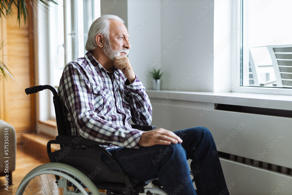 Thoughtful senior man in a wheelchair looking through window from home Thoughtful senior man in a wheelchair looking through window from home