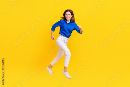 Full length photo of excited charming girl dressed blue shirt hurrying jumping high isolated yellow color background