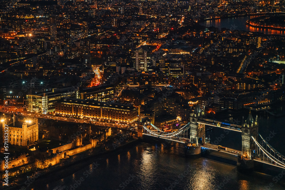 Aerial night view of Tower Bridge over river Thames, illuminated buildings glowing in dark