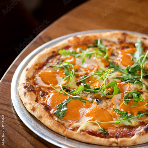 Italian pizza with cheese, ham, sauce and arugula baked intraditional way in oven. Ready dish on metal plate on wooden table. Dark background. View from above. Soft focus. Copy space. 