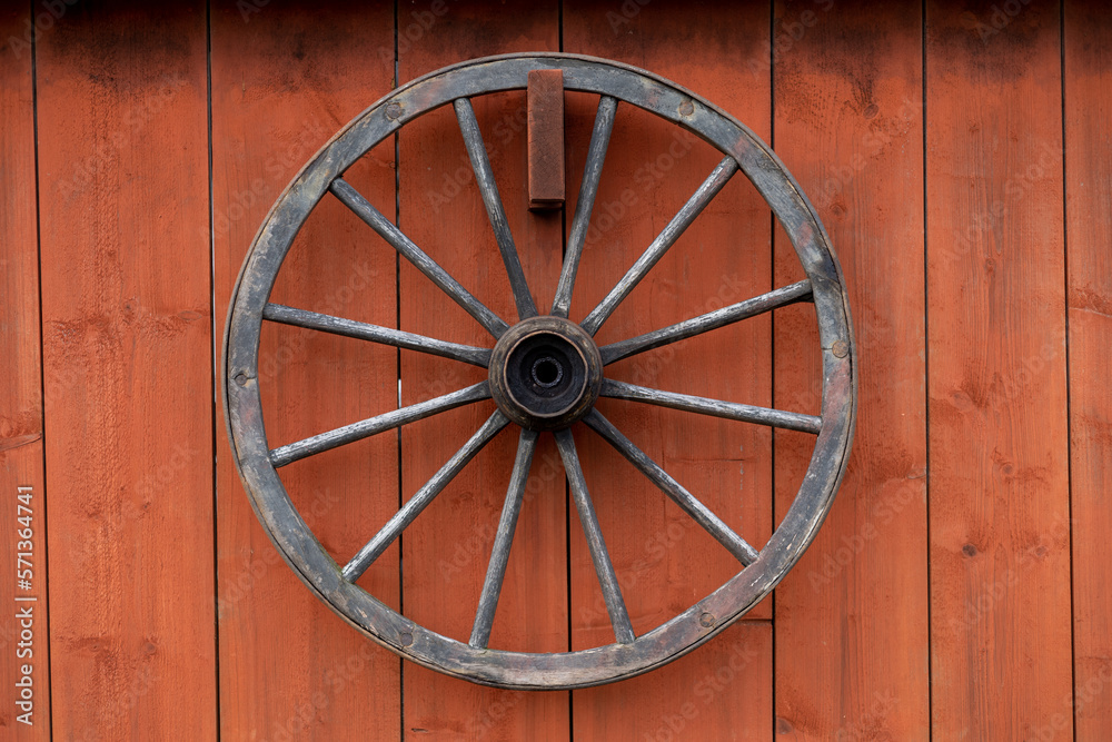 old wooden wagon wheel hanging on a red barn wall old wooden wagon wheel hanging on a red barn wall