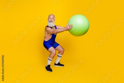 Full length photo of cheerful man professional fitness coach doing squats preparing cross marathon isolated on yellow color background © deagreez