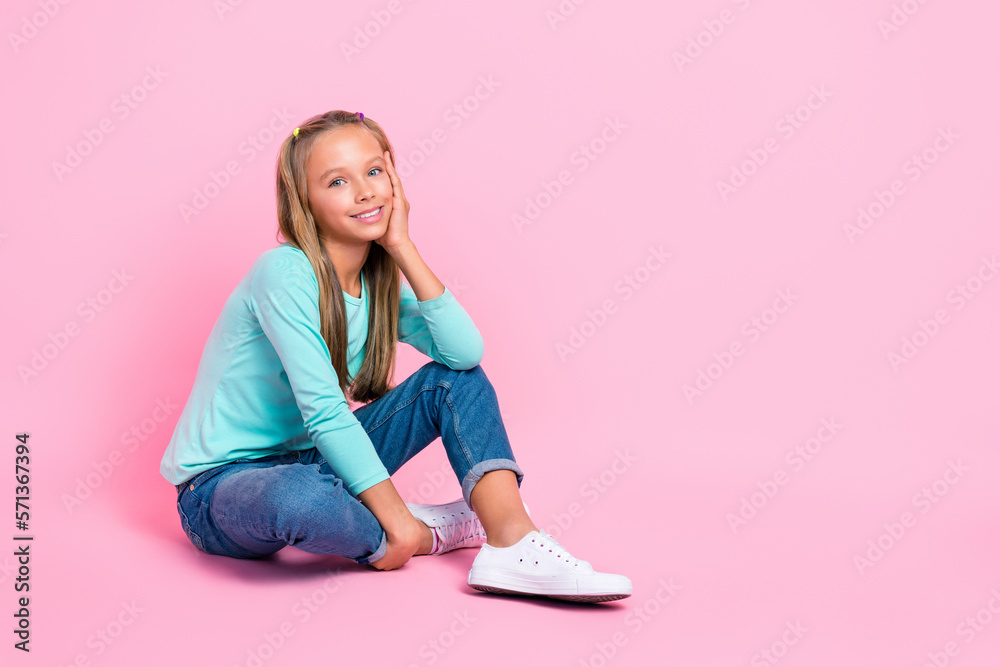 Full size photo of positive nice girl sit floor arm touch cheek empty space isolated on pink color background Full size photo of positive nice girl sit floor arm touch cheek empty space isolated on pink color background