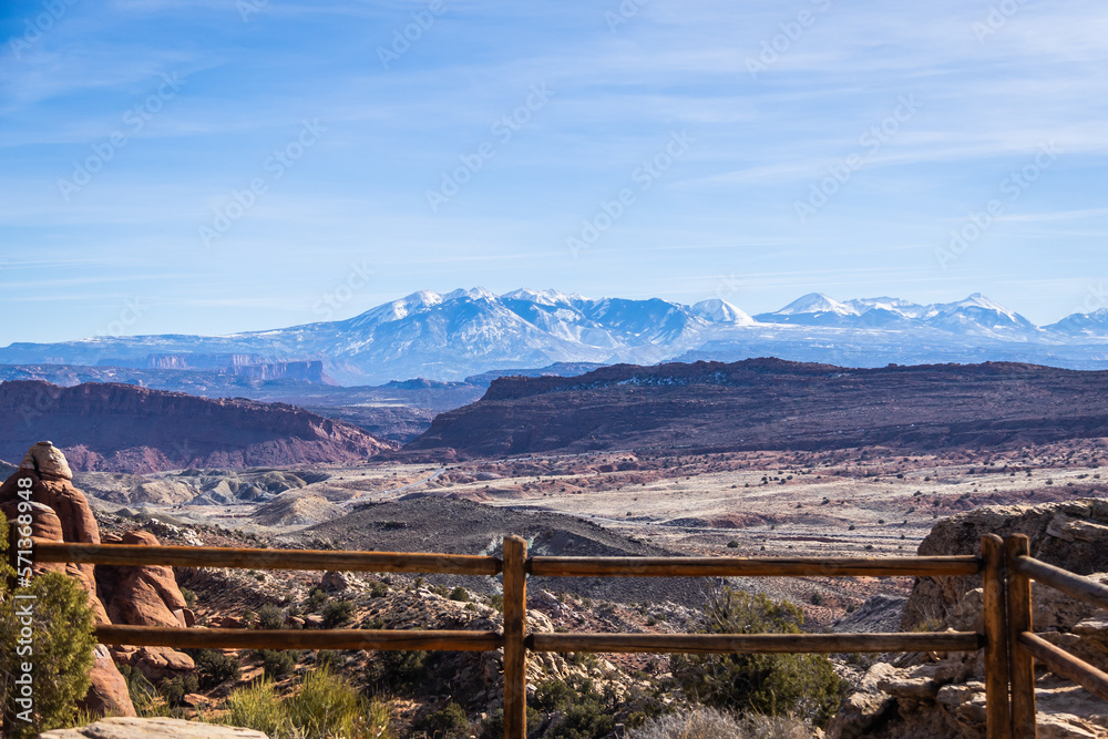 Rock formations with distant snow-covered mountains in the distance in Arches National Park with a fence.