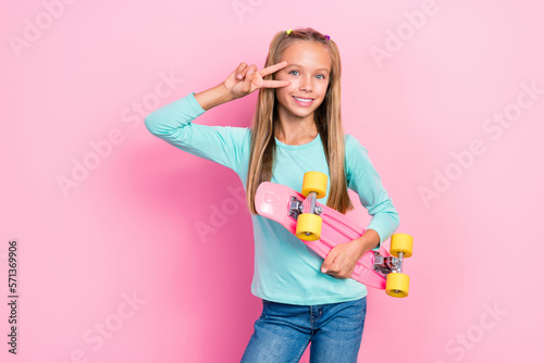 Photo of little youngster preteen schoolgirl toothy smile positive cover face fingers v-sign excited nice hold skate isolated on bright pink color background