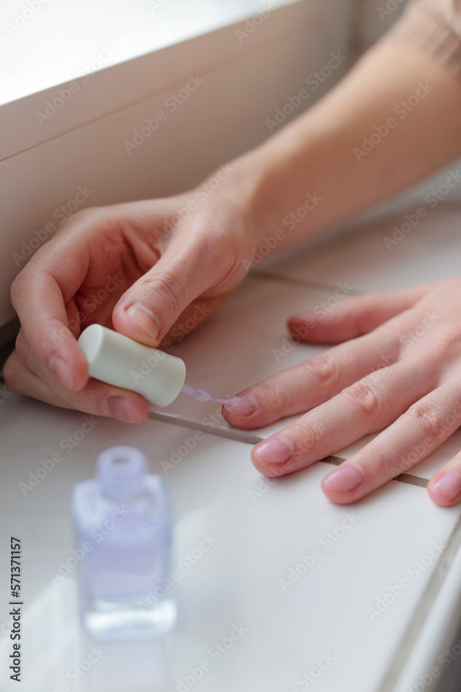 Woman paints her nails with transparent vegan nail polish.
