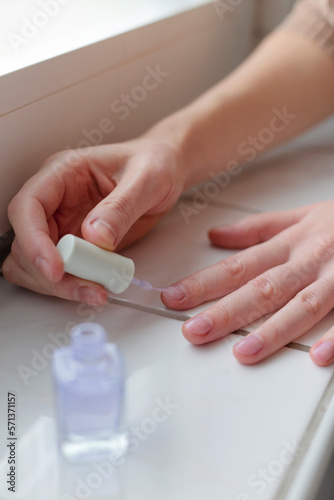 Woman paints her nails with transparent vegan nail polish.