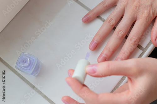 Woman paints her nails with transparent vegan nail polish. Eco self care.