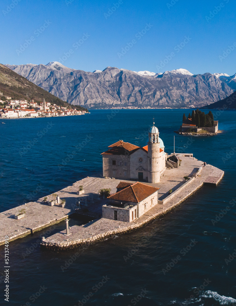 Aerial drone view of Gospa Od Skrpjela island, our Lady of the Rocks church, Montenegro, Boka Bay and Adriatic sea, with Perast town and island of Saint George in the background in a sunny day