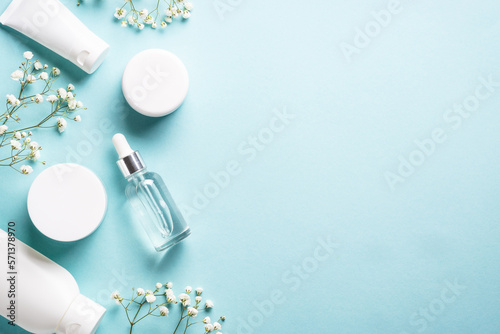 Natural cosmetic products at blue background. Cream, serum, tonic with green leaves and flowers. Flat lay image with copy space.