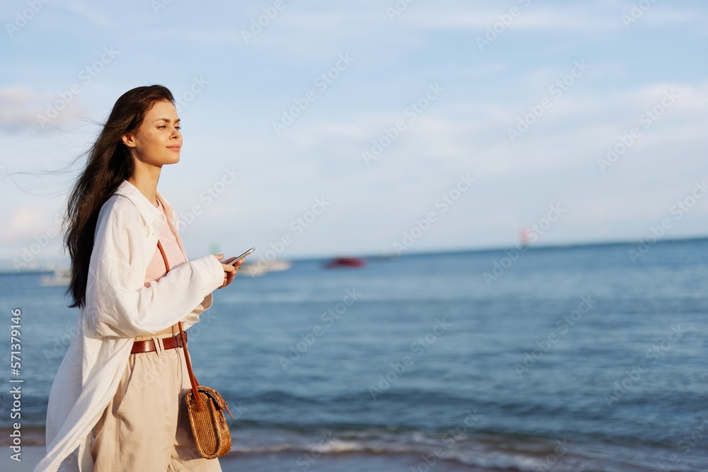 Freelance woman with phone in hand on vacation walking on the beach by the ocean in Bali, happy travel and vacation, mobile communications, Internet online Freelance woman with phone in hand on vacation walking on the beach by the ocean in Bali, happy travel and vacation, mobile communications, Internet online