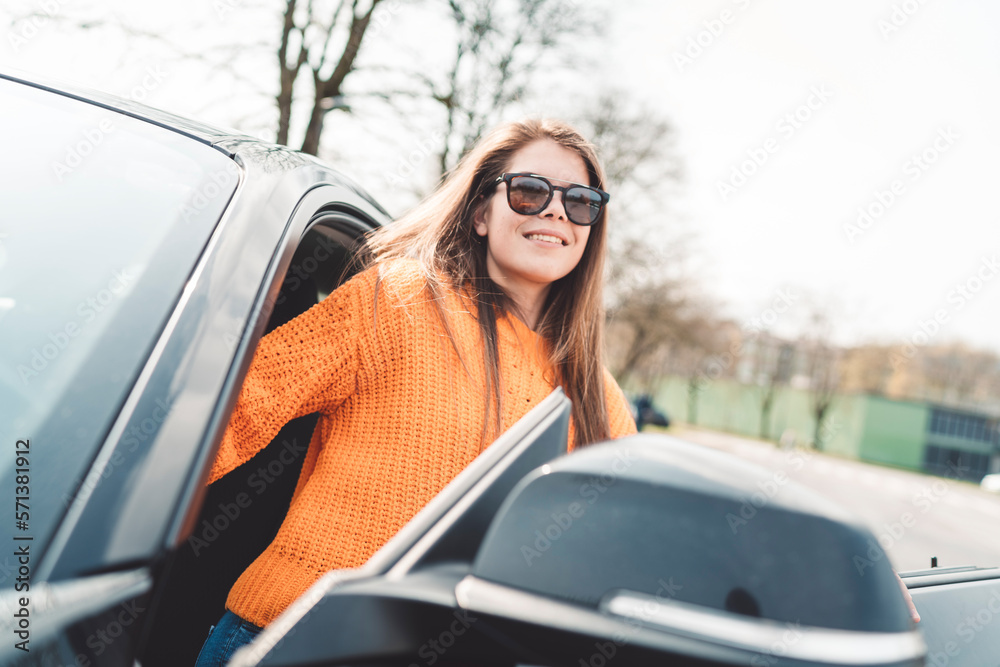 Young woman with long brown hair and big smile on her face stepping out of a black car on a sunny day Young woman with long brown hair and big smile on her face stepping out of a black car on a sunny day